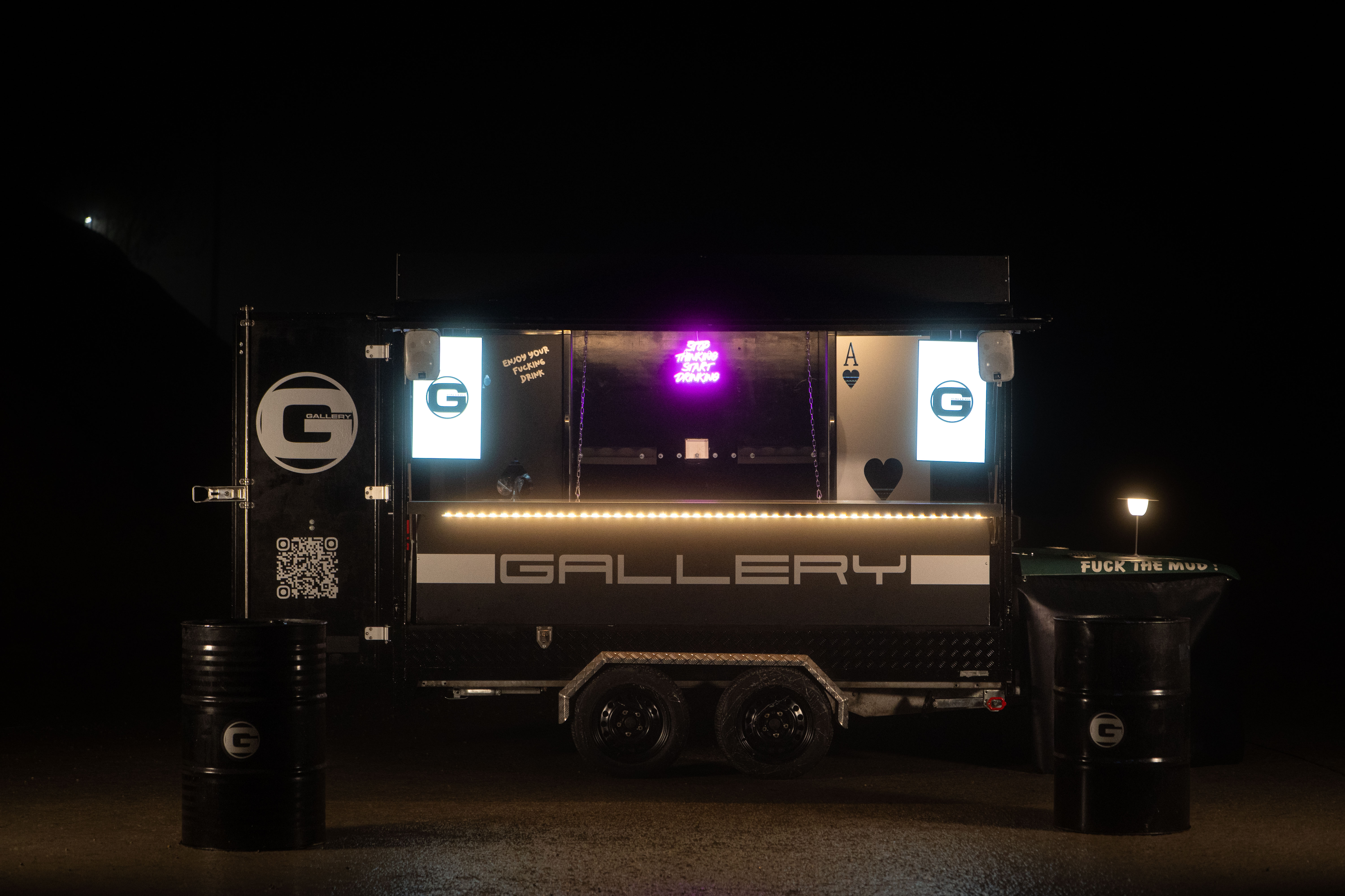 Der beleuchtete Gallery Barwagen bei Nacht mit zwei Stehtischen